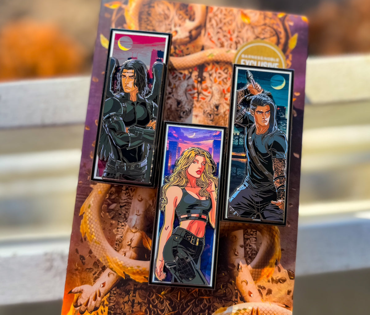Three illustrated pins featuring characters on a decorative book with a snake design.