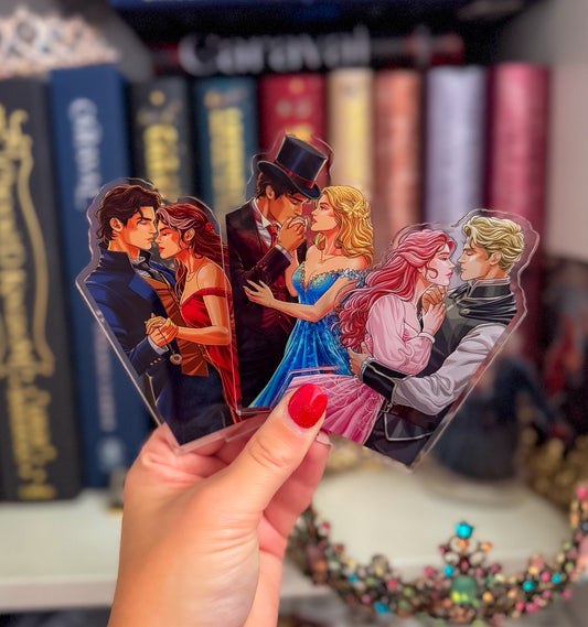 A hand with red nail polish holds a set of four die-cut acrylic bookmarks or tags featuring illustrated romantic couple scenes, with blurred book spines in the background.