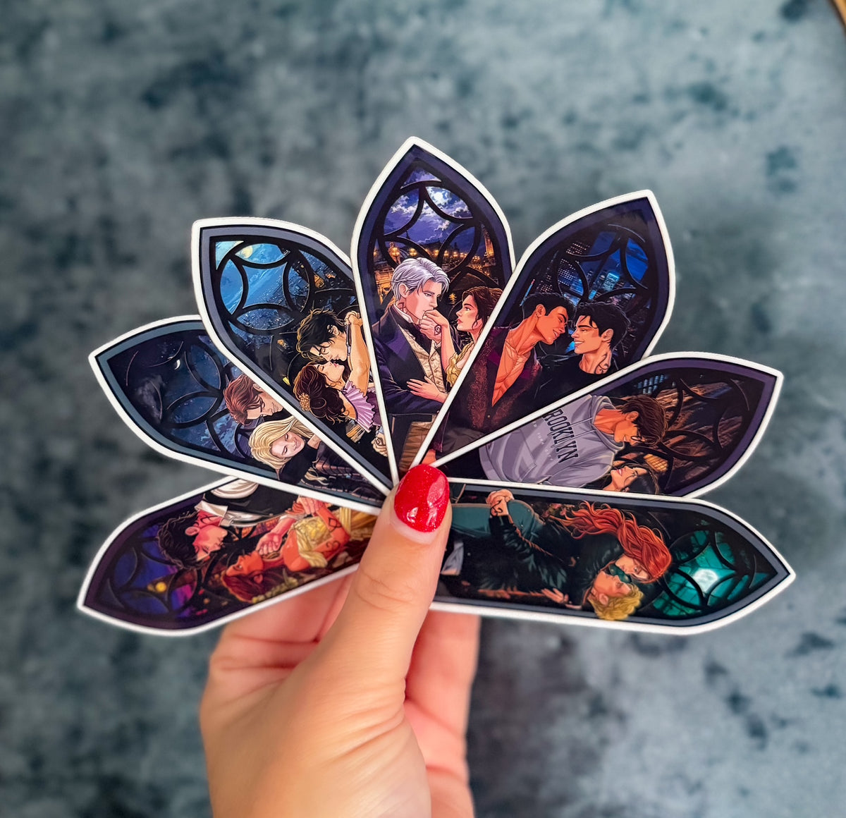 A hand with red nail polish holds a die-cut sticker shaped like a lotus flower, featuring colorful anime-style stained-glass panels. The background is a textured gray surface.
