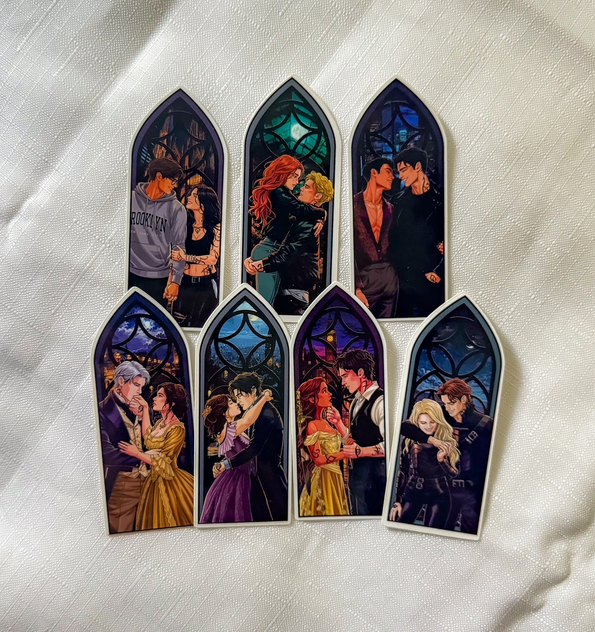 Seven arched window-shaped stickers featuring romantic illustrated couples in stained-glass-style scenes, arranged on a white textured fabric background.